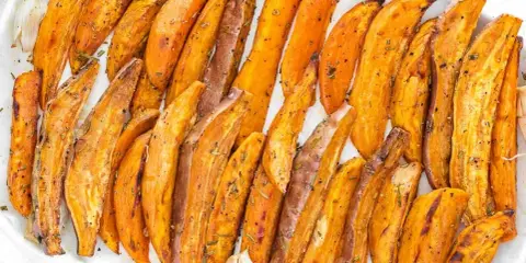 Patate dolci al forno, tagliate a spicchi e condite con erbe aromatiche, servite su un piatto bianco.