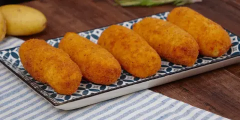 Cinque crocchette di patate dorate e croccanti su un piatto decorato, pronte per essere gustate.