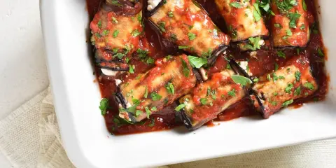 Involtini di melanzane ripieni di formaggio, cotti in sugo di pomodoro e guarniti con prezzemolo fresco.