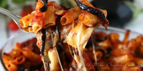 Un primo piatto fumante di pasta alla norma, con melanzane fritte, pomodoro e tanto formaggio filante che si allunga.