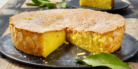 Una deliziosa caprese al limone, cosparsa di zucchero a velo e scorzetta d'arancia, con mandorle sui bordi.
