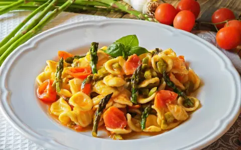 Piatto di orecchiette con asparagi freschi e pomodorini succosi, guarnito con basilico. Un classico della cucina italiana.