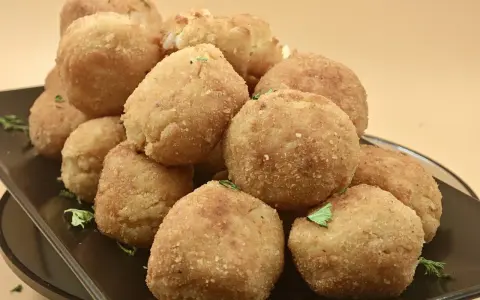 Un mucchio invitante di polpette di riso dorate e croccanti, guarnite con prezzemolo fresco, su un piatto scuro.