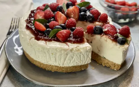 Deliziosa torta fredda allo yogurt, guarnita con fragole, lamponi, mirtilli e una colata di marmellata. Perfetta per un dessert estivo.