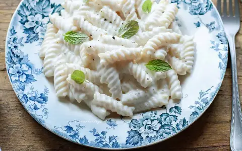 Fusilli cremosi conditi con una salsa vellutata alla ricotta, guarniti con foglie di menta fresca su un piatto decorato.