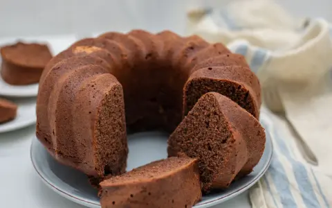 Un soffice ciambellone al cioccolato, appena sfornato, con alcune fette già pronte per essere gustate.