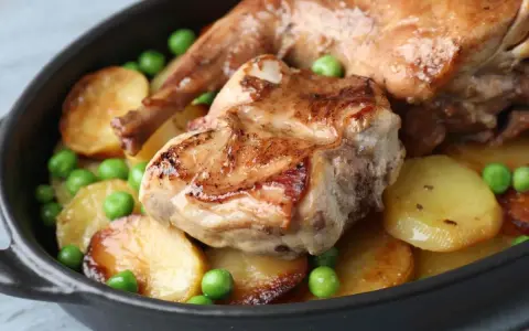 Un saporito coniglio in umido con patate arrosto e piselli verdi, servito in una cocotte scura.