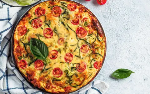 Torta salata vegana con zucchine e pomodorini, guarnita con basilico fresco.