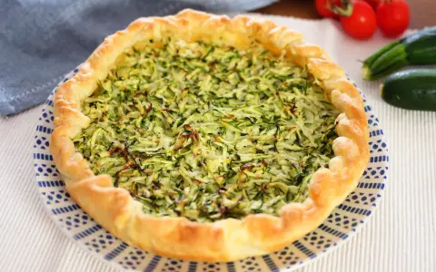 Torta salata con zucchine grattugiate e ricotta, con bordo dorato e decorazione blu su piatto bianco.