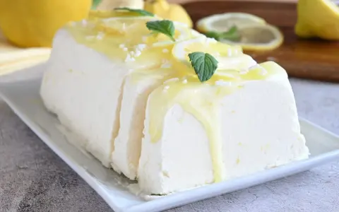 Un delizioso semifreddo al limone, guarnito con scorzette, menta e una glassa gialla, pronto per essere gustato.