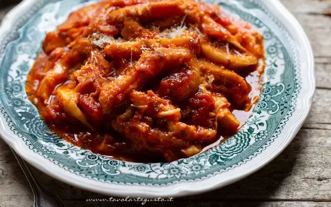 Un piatto fumante di trippa alla romana, ricca di sugo di pomodoro e condita con pecorino grattugiato, servita su un piatto decorato.