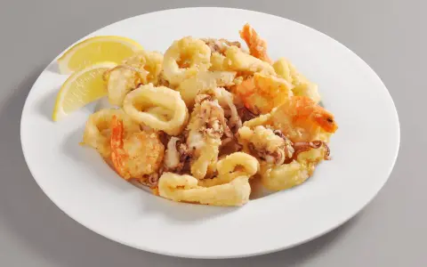 Un invitante piatto di frittura di pesce, con anelli di calamari dorati e gamberi croccanti, guarnito con spicchi di limone fresco.