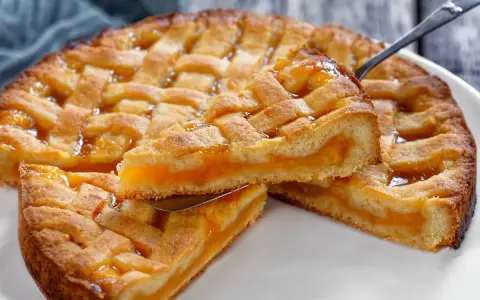 Una fetta di crostata senza glutine con ripieno di albicocche dorate, la sua pasta friabile e la griglia decorativa invitano a un assaggio goloso.