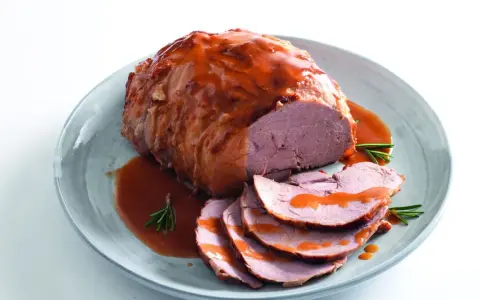 Un succulento arrosto di manzo, affettato e nappato con salsa, servito su un piatto con rosmarino.