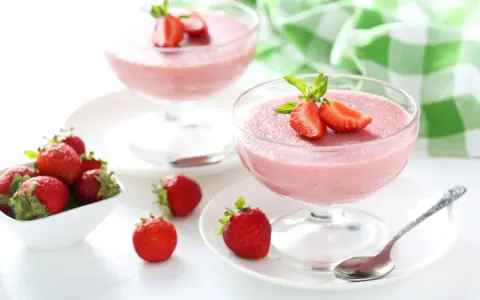 Deliziosa mousse di fragole in coppette di vetro, guarnita con fragole fresche e menta. Accanto, fragole in una ciotola bianca.