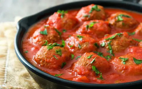 Polpette di carne succulente in salsa di pomodoro, guarnite con prezzemolo fresco, servite in una padella di ghisa.