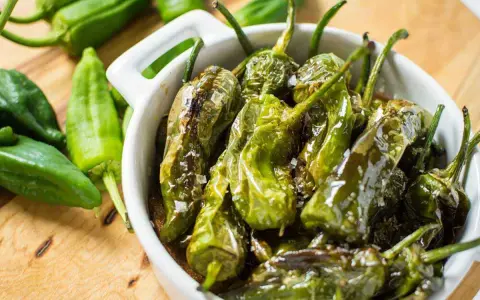 Friggitelli in padella, cotti e lucidi, cosparsi di sale grosso, in una ciotola bianca.