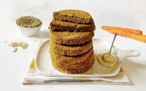 Impilati hamburger di lenticchie dorati, con lenticchie secche, carote e una salsa cremosa in un piatto.