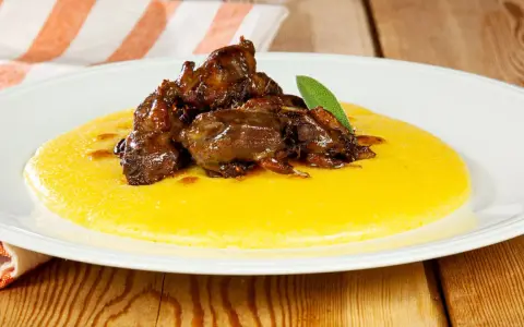 Piatto di polenta e osei, con uccellini scuri in umido e una foglia di salvia.