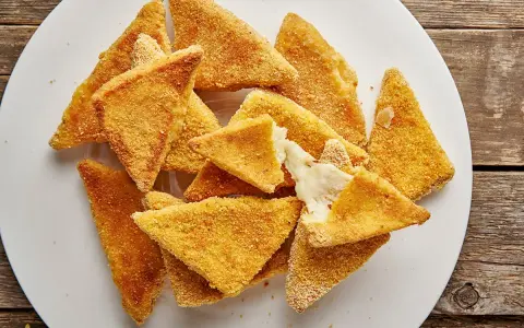 Mozzarella in carrozza al forno, triangolini dorati e croccanti con cuore filante di formaggio fuso, serviti su un piatto bianco.