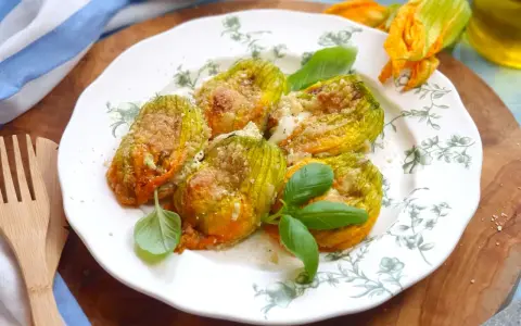 Deliziosi fiori di zucca al forno, ripieni e dorati, guarniti con basilico fresco su un piatto decorato.