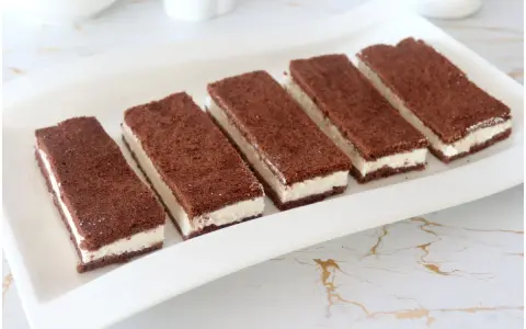 Sei fette di torta kinder fetta al latte, con pan di spagna al cacao e crema bianca, disposte su un piatto bianco.