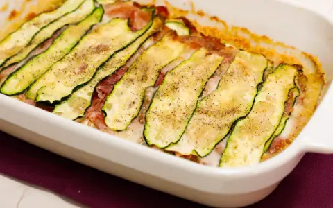 Sformato di zucchine appena sfornato, con fette sottili di zucchina grigliata, prosciutto e formaggio filante, condito con pepe nero.