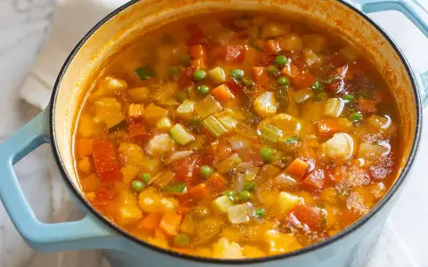 Un fumante minestrone di verdure in una pentola azzurra, ricco di carote, zucchine, piselli e pomodoro.