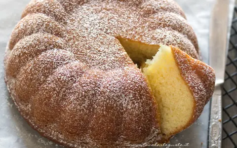 Torta 7 vasetti soffice e dorata, spolverata di zucchero a velo. Una fetta è stata tagliata, rivelando l'interno profumato.