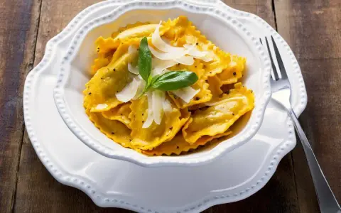 Un piatto invitante di tortelli di zucca, guarniti con scaglie di parmigiano e una fogliolina di basilico, pronti per essere gustati.