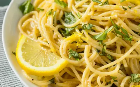 Spaghetti al limone cremosi, guarniti con scorza di limone e basilico fresco. Un piatto invitante e profumato.