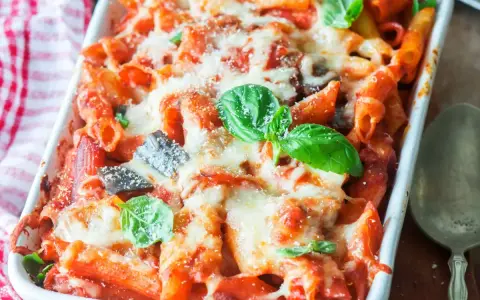 Piatto fumante di pasta al forno con melanzane, ricoperta di formaggio fuso e basilico fresco.