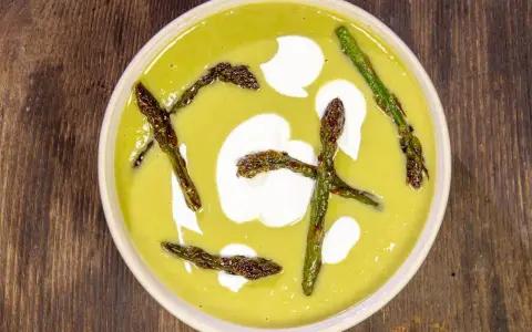 Crema di asparagi vellutata, guarnita con asparagi croccanti e un tocco di panna.