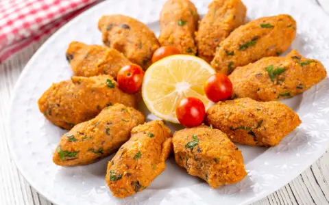 Deliziose polpette di lenticchie, disposte a cerchio su un piatto bianco, con spicchi di limone e pomodorini ciliegino.