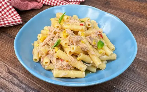 Piatto di pasta tonno e limone, condita con tonno sfilacciato, scorza di limone e basilico fresco, servita in un piatto blu.