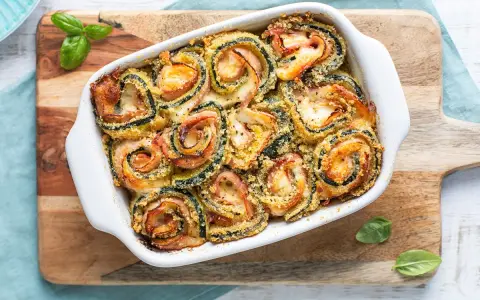 Involtini di zucchine al forno, ripieni di prosciutto e formaggio, dorati e croccanti, guarniti con basilico fresco.
