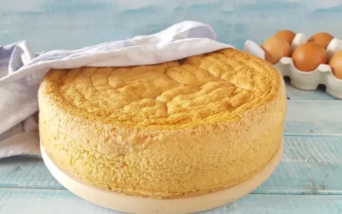 Un soffice pan di spagna dorato, coperto da un canovaccio, con uova fresche sullo sfondo.