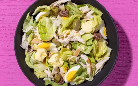 Insalata di pollo ricca con lattuga, uova sode, olive verdi e acciughe, condita con maionese.