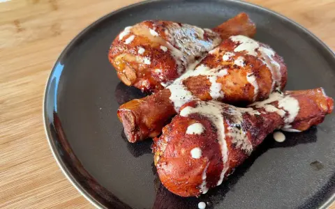 Tre succulenti fusi di pollo arrostiti, conditi con spezie e nappati con una cremosa salsa bianca, serviti su un piatto scuro.