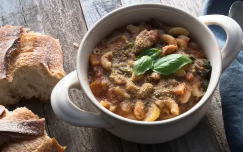 Una ciotola di pasta e fagioli in scatola, guarnita con basilico fresco e pane croccante su un tavolo di legno.