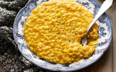 Un cremoso risotto alla zucca, servito su un piatto decorato, con una forchetta che affonda nel piatto.