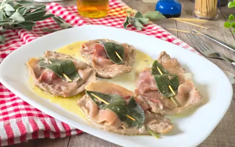 Saltimbocca alla romana: fettine di vitello con prosciutto e salvia, servite su un piatto bianco con salsa dorata.