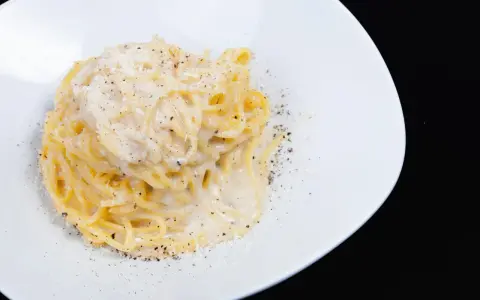 Un piatto di spaghetti cacio e pepe, cremosi e ricchi, cosparsi di pepe nero macinato fresco e formaggio grattugiato.