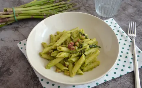 Penne cremose con asparagi freschi e cubetti di speck croccante, un piatto primaverile gustoso.