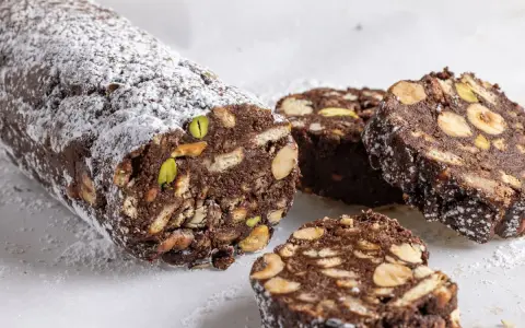 Salame di cioccolato senza uova ricetta della nonna, con biscotti, nocciole e pistacchi, spolverato di zucchero a velo.