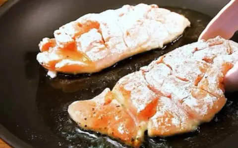 Due filetti di petto di pollo infarinati cuociono in padella, sfrigolando nell'olio caldo.