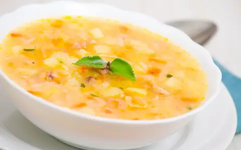 Una ciotola di zuppa cremosa con pezzi di patate e riso, guarnita con una foglia verde. Un piatto confortante che sa di casa.