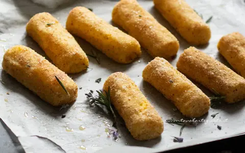 Crocchette di patate al forno dorate e croccanti, adagiate su carta forno con rametti di rosmarino e fiori di lavanda.