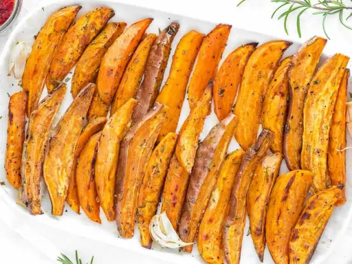 Patate dolci al forno, tagliate a spicchi e condite con erbe aromatiche, servite su un piatto bianco.