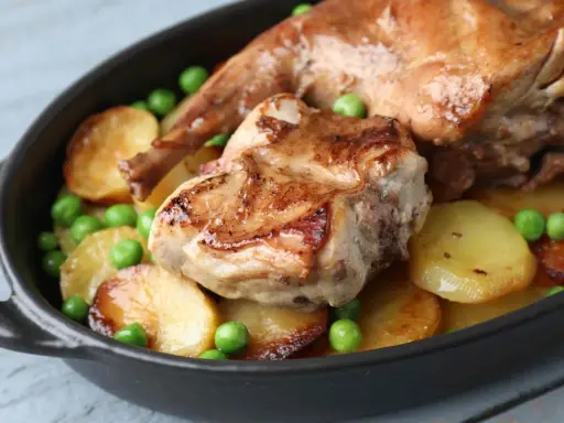 Un saporito coniglio in umido con patate arrosto e piselli verdi, servito in una cocotte scura.